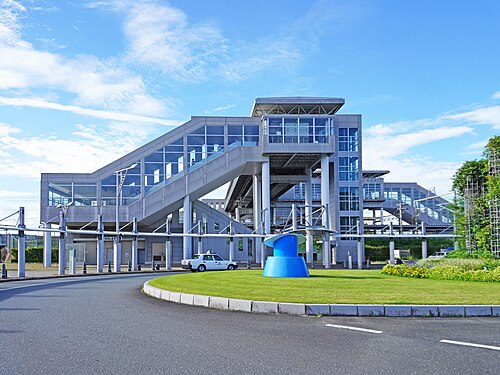 愛野駅南口の階段とガラス張りの駅舎、手前のロータリーと芝生