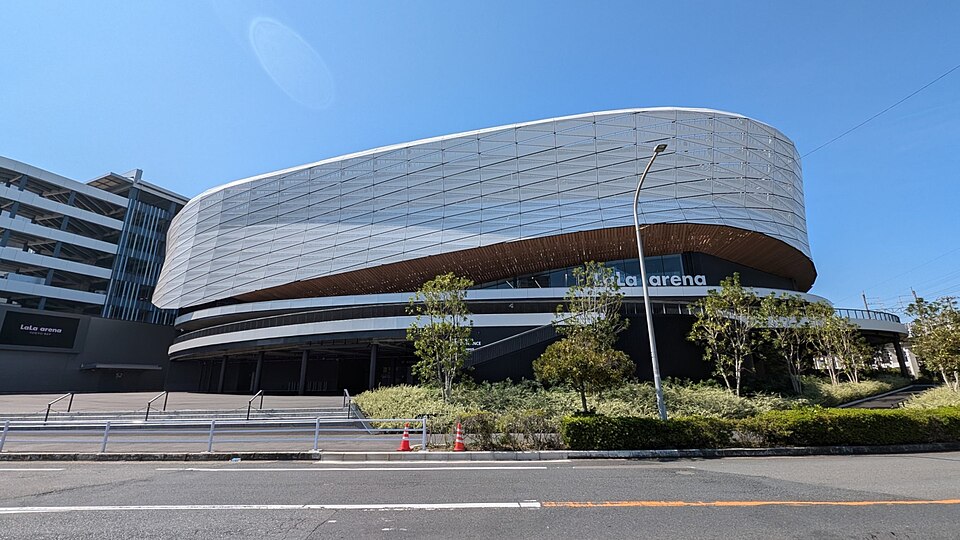 白い曲面の外壁にLaLa arenaの文字がある建物と、前を通る道路や植栽