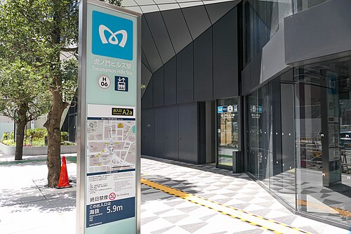 日比谷線H06とA2aを示す看板が立つ、虎ノ門ヒルズ駅のガラス張りの出入口と歩道