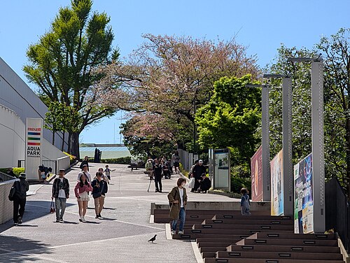 マクセルアクアパーク品川の看板沿いに広がる歩行者通路と植栽、歩いている人たち