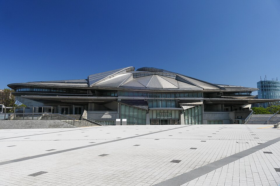 曲面の屋根と大きな前庭、その奥に入口がある東京体育館メインアリーナ